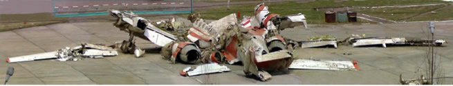 A reassembled plane wreckage on the tarmac as seen from behind. The left wing is on the left.